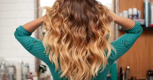 A woman with long, wavy hair styled in highlighted tight blonde curls at a salon, showcasing her vibrant hairstyle.