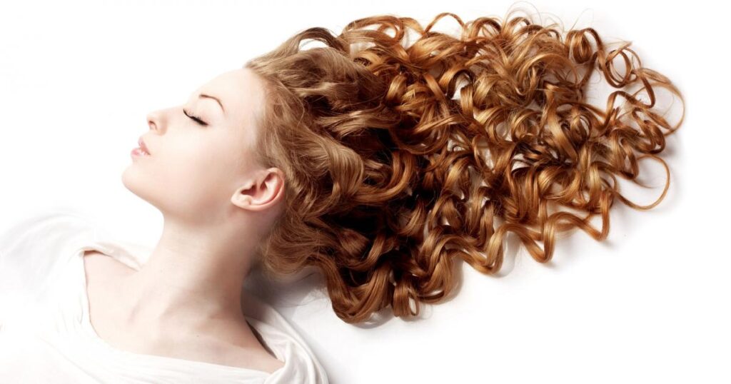 A woman with feathery curls is lying down, showcasing her beautiful, textured hairstyle in a relaxed position.