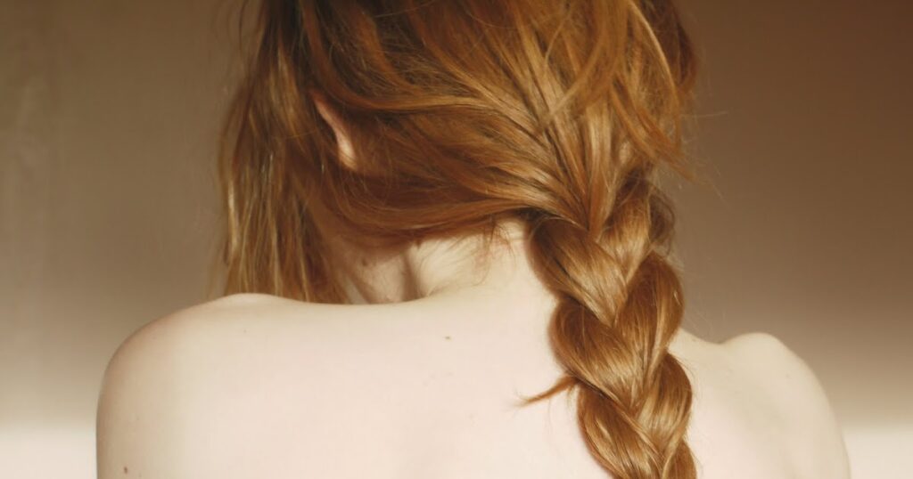 A woman with long red hair styled in beautiful undone braids, showcasing a relaxed and elegant look.